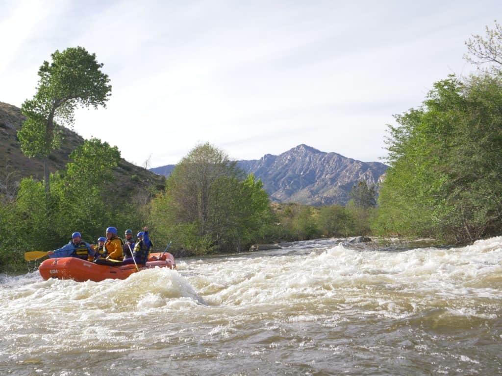 class II waves as a group of rafters floats down the river with mountains in the background Sierra South Mountain Sports Kern River California