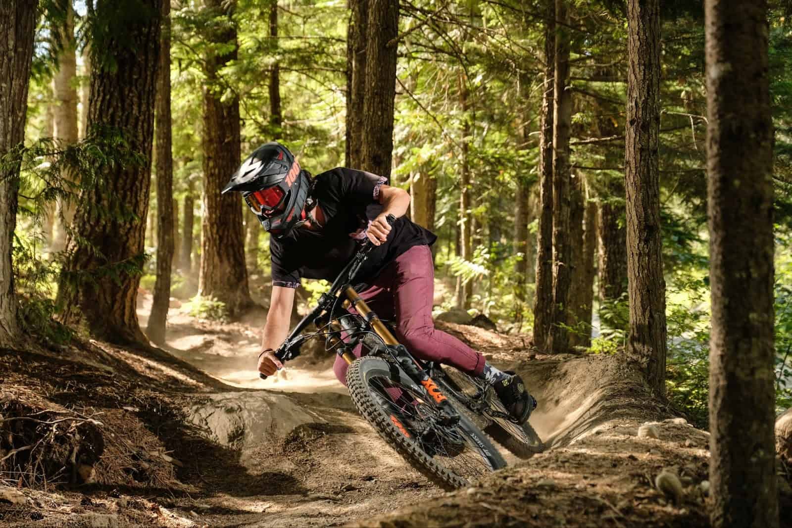 Person with full face helmet riding mountain bike through a forest path